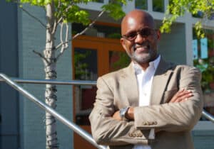 A black man stands before a building, representing God's restoration of Cornelius Williams through DVULI.