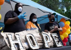 Group of masked people gather for Claudia's House at Atlanta's Grove Park, offering food and aid. LaTonya Gates leads the community.