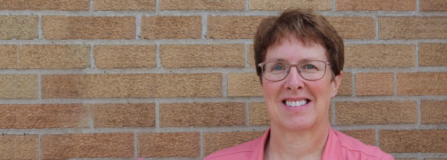 A smiling woman in front of a brick wall welcomes Denise Fase, a new part-time staff liaison for DVULI.