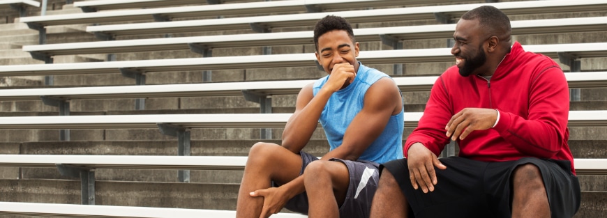 Two men sit on bleachers in a stadium, discussing mending the fatherless fracture through mentorship, an opinion by Jon Coker.