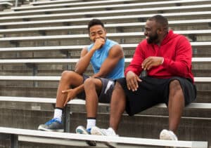 Two men mentor on stadium bleachers, bridging the fatherless gap for at-risk youth in San Antonio.