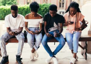 A group of young people looking at their phones navigate tough topics with tomorrow's leaders through Crucial Conversations with Gen Z.