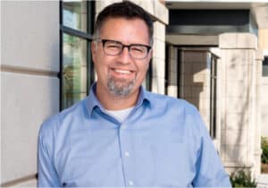 A man wearing glasses and a blue shirt, Ryan VerWys leads ICCF in equitable housing and neighborhood development.