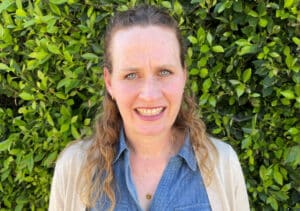 Jennifer Hicks, Executive Director at Neighborhood Homework House, stands smiling in front of a hedge.