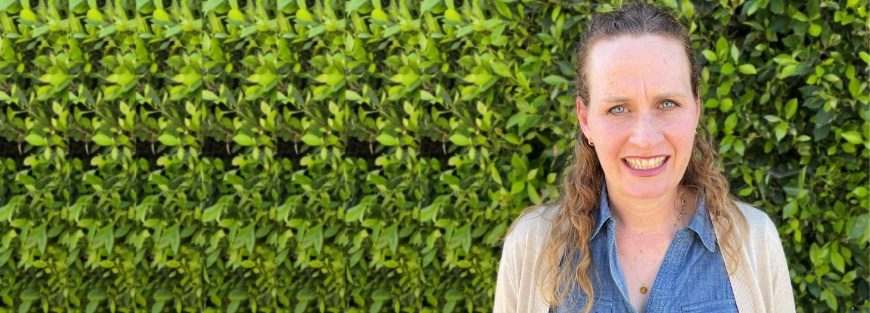 Alumni Jennifer Hicks, executive director of Neighborhood Homework House, smiles in front of a hedge.