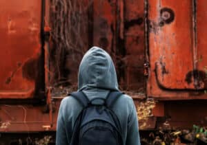 A man in a hoodie stands before a rusty train car in Brandon Woodard's "Confronting Housing Insecurity Among Urban Youth".