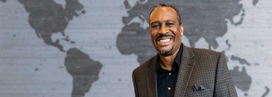 Alvin Sanders, World Impact President, leads with humility and self-awareness. Gerald Bell's 2003 portrait shows him smiling in front of a world map.